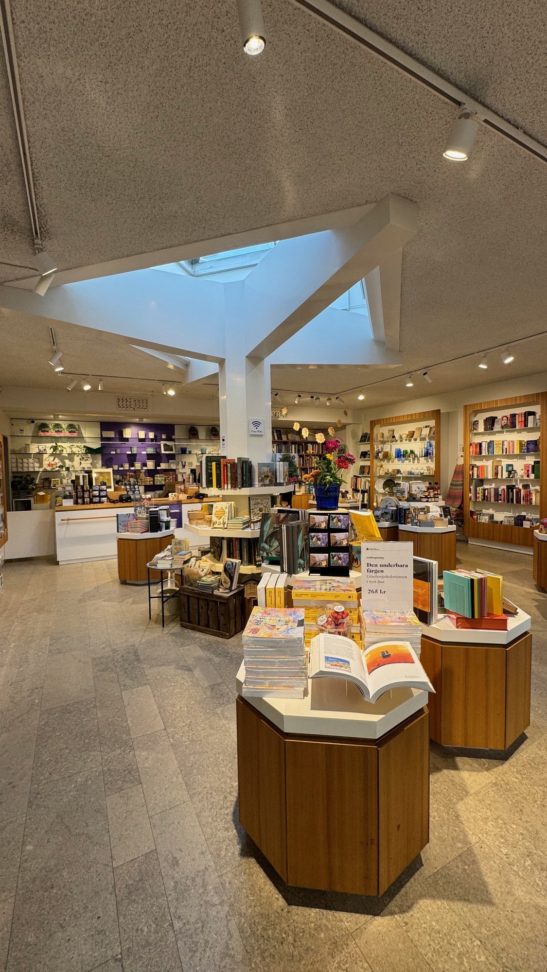 The museum shop at Waldemarsudde with books, cards and gifts on wooden tables under a skylight.