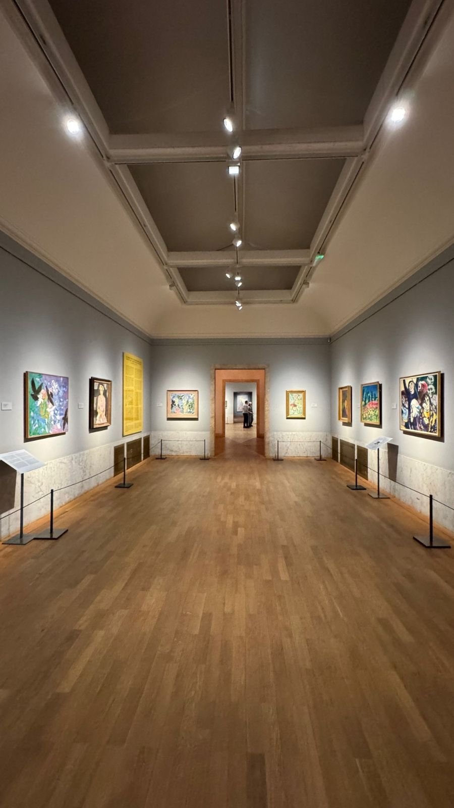 A long view through gallery rooms with grey walls, colorful paintings and a wooden floor at Waldemarsudde.