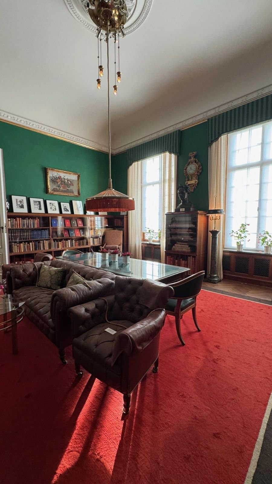 A library room in the Waldemarsudde mansion with green walls, bookshelves, leather chairs and a red carpet.
