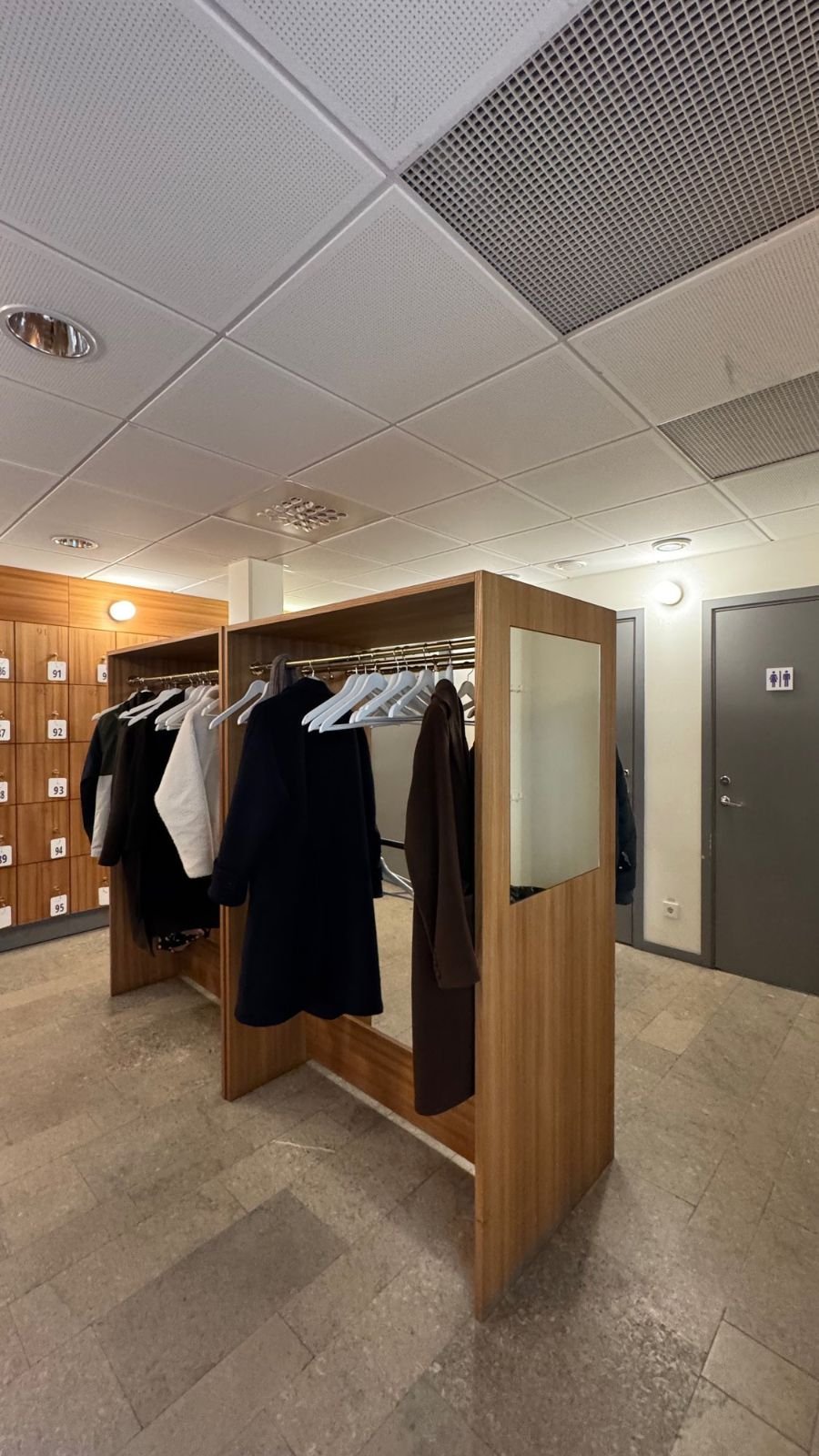 The cloakroom at Waldemarsudde with coat racks, wooden lockers and a toilet door with a sign.