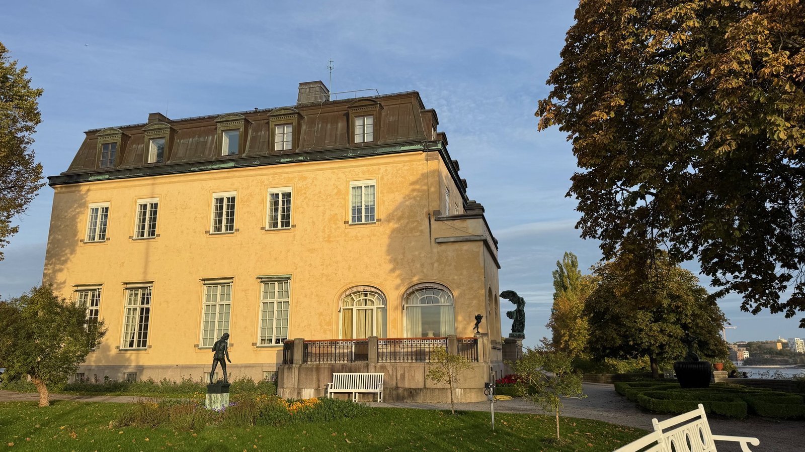 The yellow mansion of Prins Eugens Waldemarsudde on Djurgården, with a lawn, sculptures and a white bench.