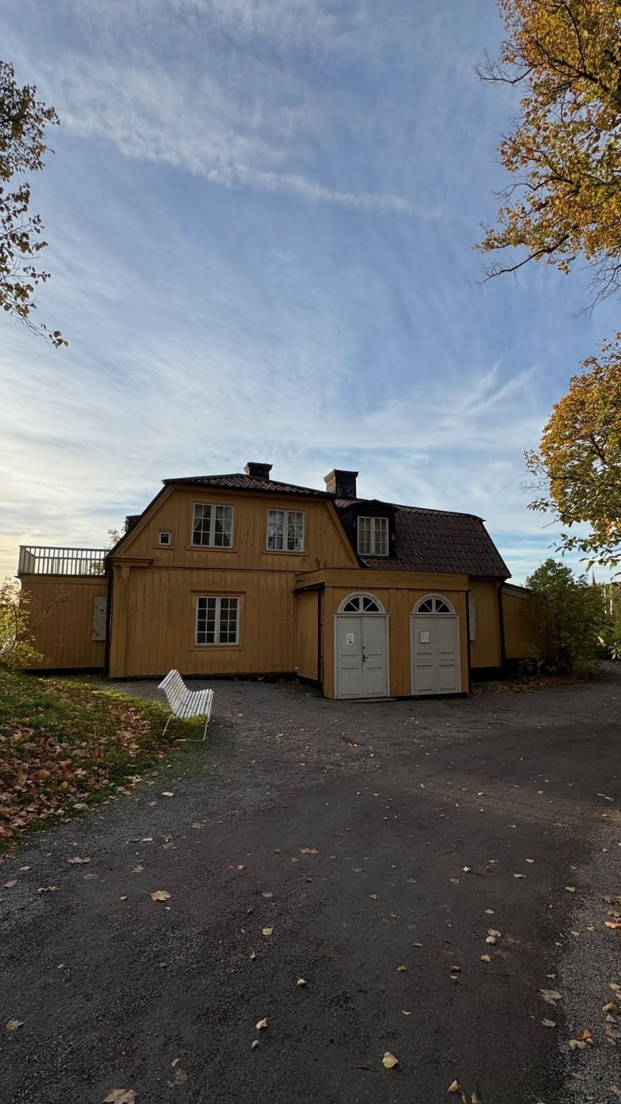 The yellow wooden Old House at Waldemarsudde with a mansard roof and a white bench.