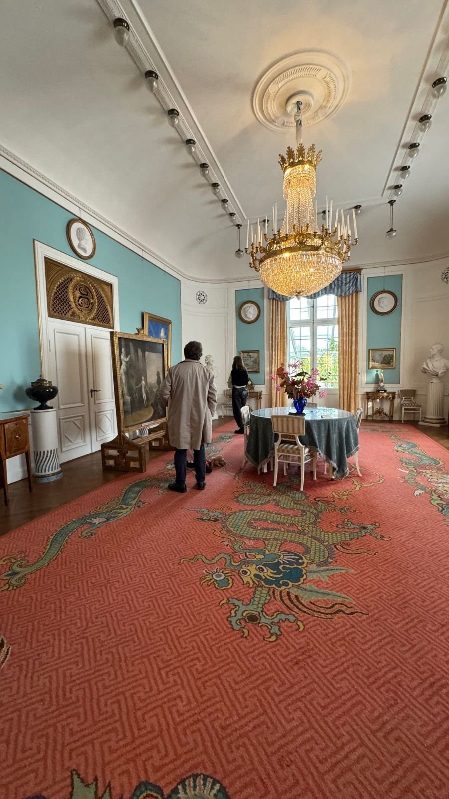 A room with light blue walls, a crystal chandelier and a red carpet with a dragon pattern at Waldemarsudde.