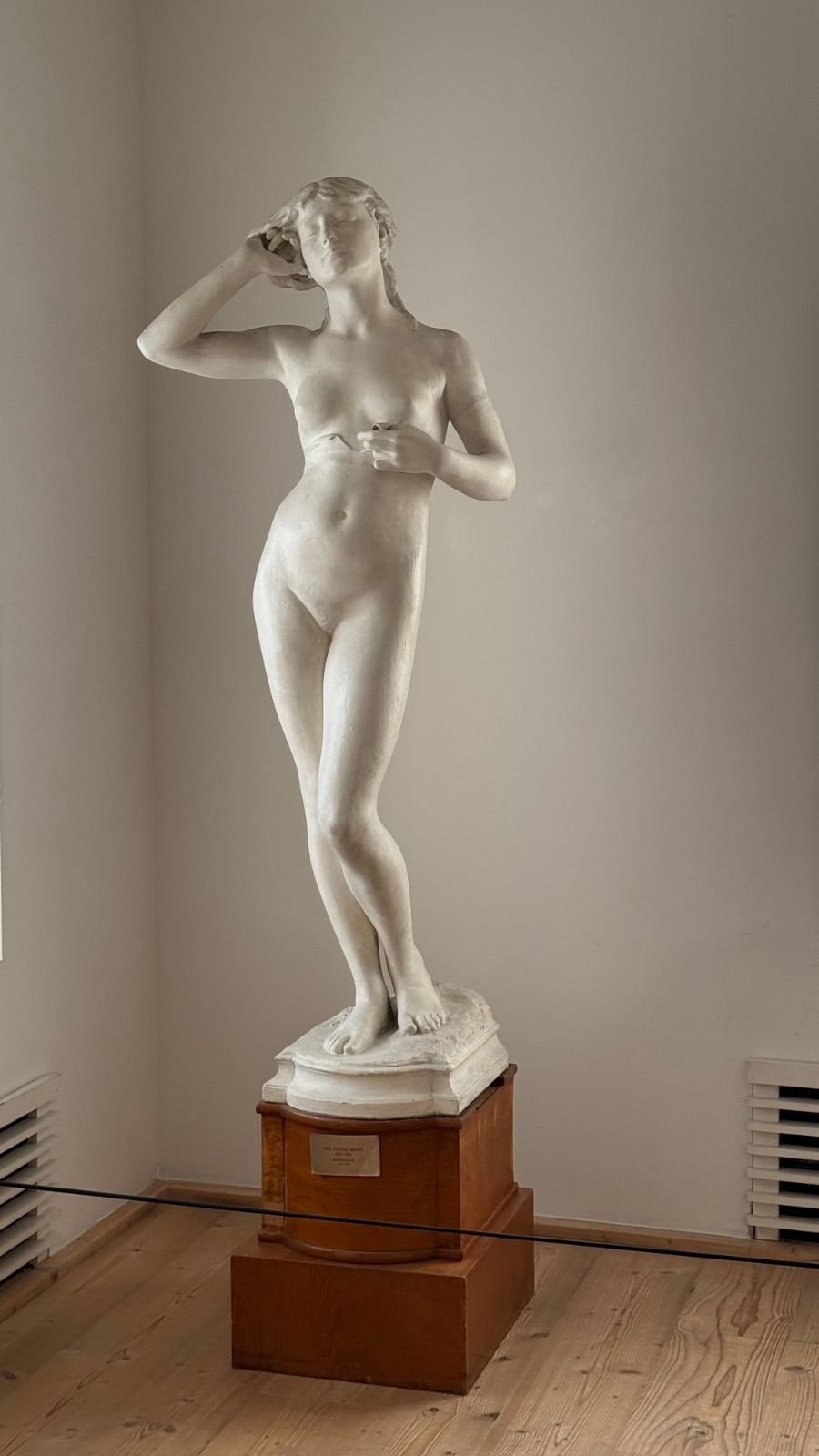 A white marble sculpture of a standing woman on a wooden pedestal at Waldemarsudde.