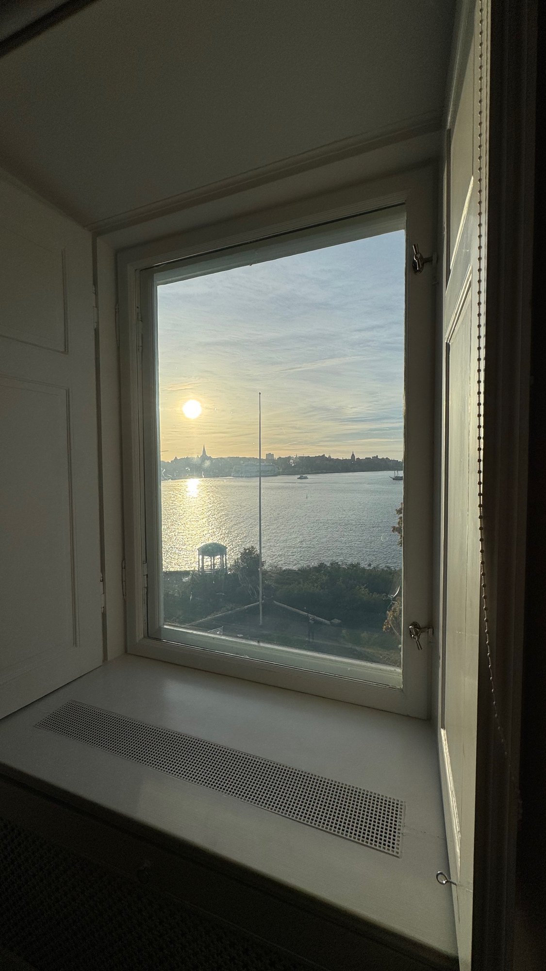 A deep window frames the sun over Saltsjön and a white pavilion at Waldemarsudde.
