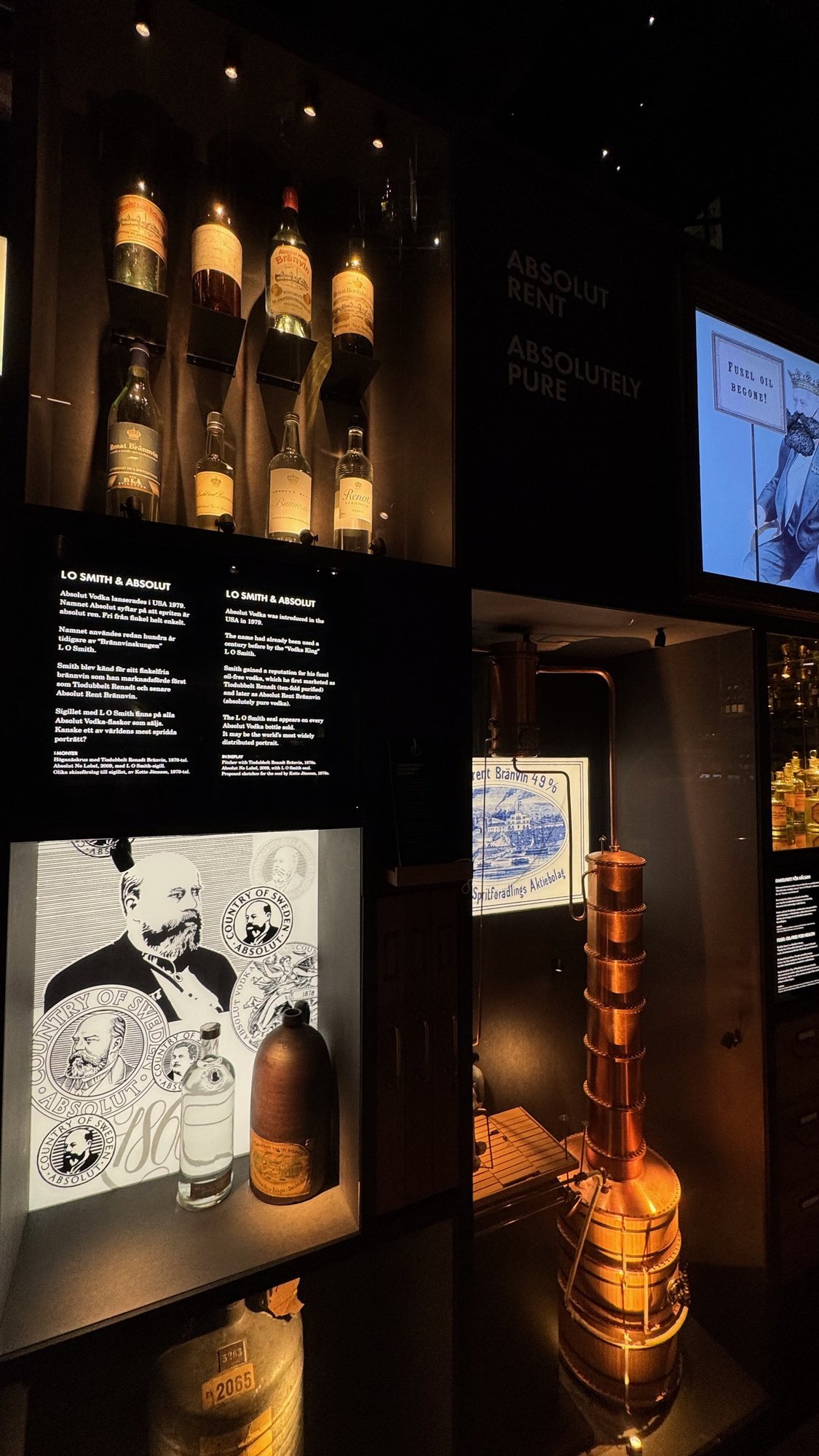 A display about L.O. Smith and Absolut at Spritmuseum with old bottles on shelves and a copper still.