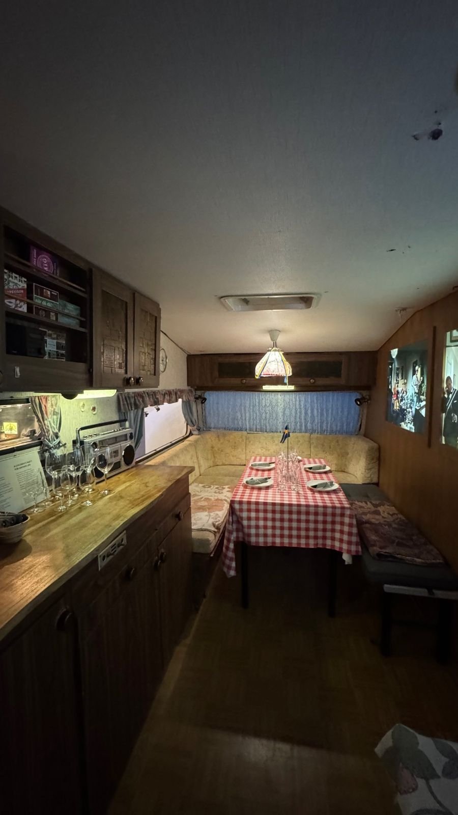 Inside an old caravan at Spritmuseum with a red checkered tablecloth, a lamp and wood-paneled cupboards.