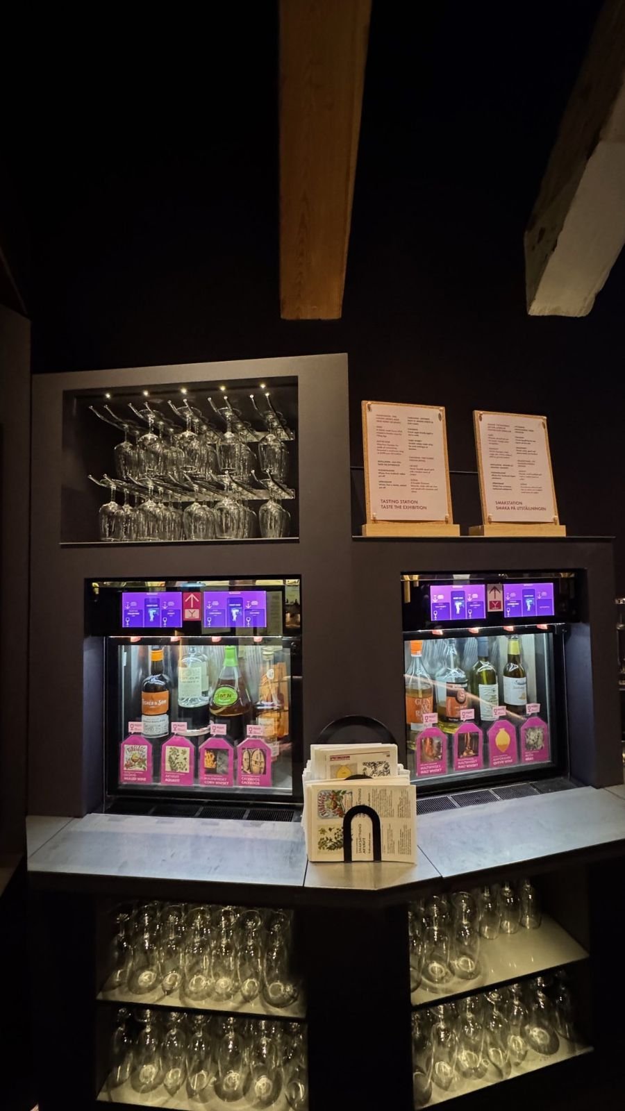 Two self-service tasting machines with bottles and rows of glasses at Spritmuseum.