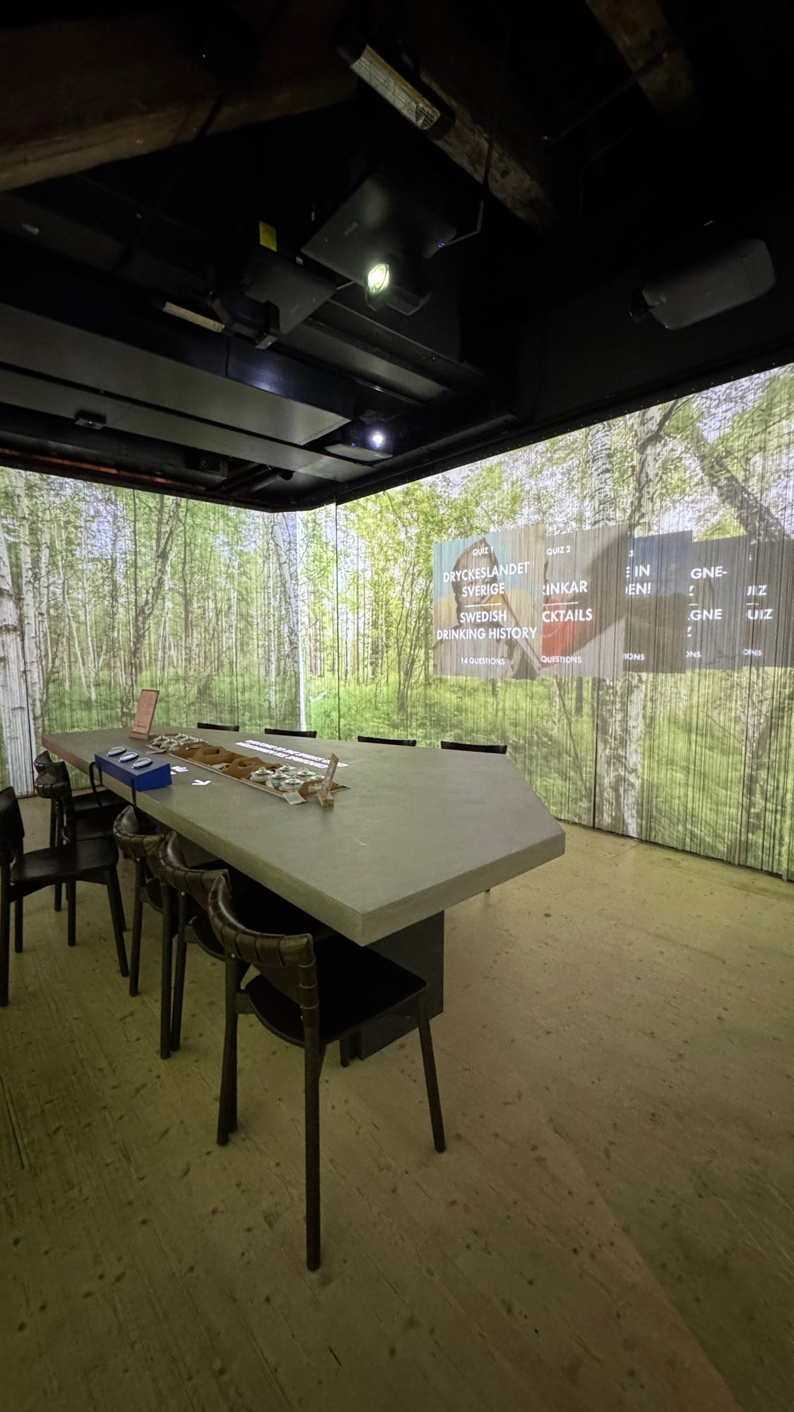 A tasting room at Spritmuseum with a long table, black chairs and a birch forest picture on the walls.