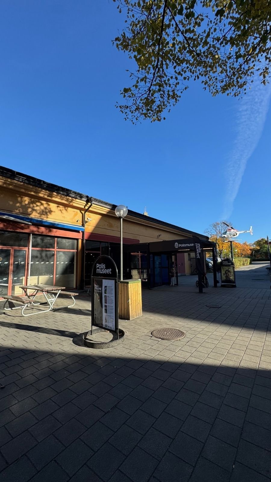 The entrance to Polismuseet with benches and a sign in the sun.