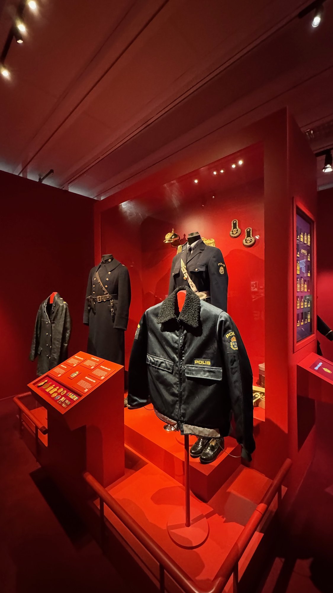 Police uniforms and a leather jacket on display in a red room at Polismuseet.