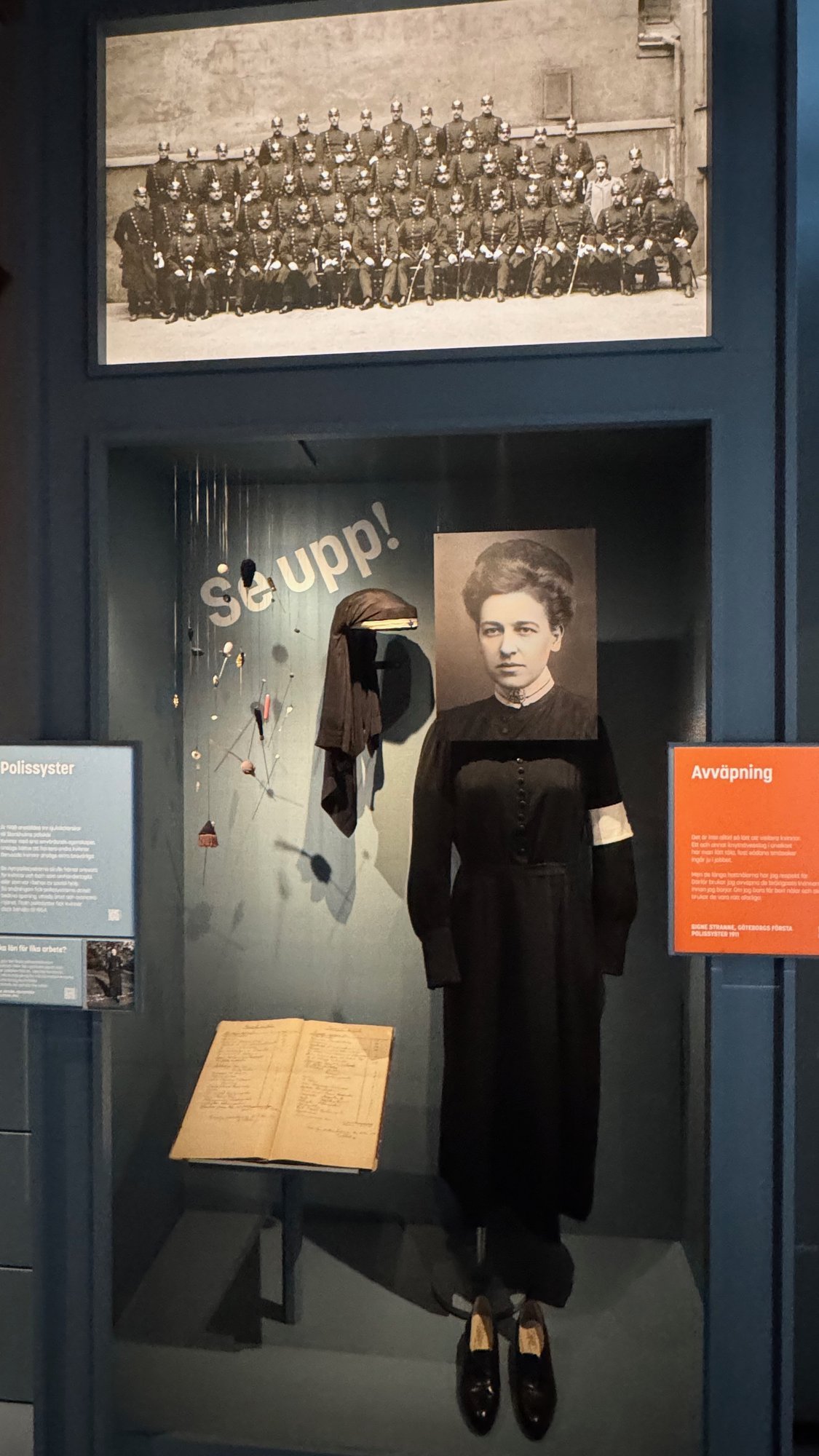 A display case with a black dress and a historic group photo of policewomen at Polismuseet.