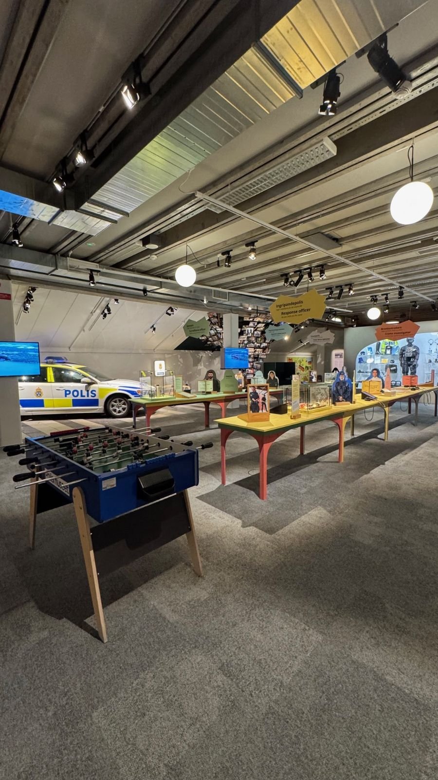 A large hall with a police car, a foosball table and activity tables at Polismuseet.