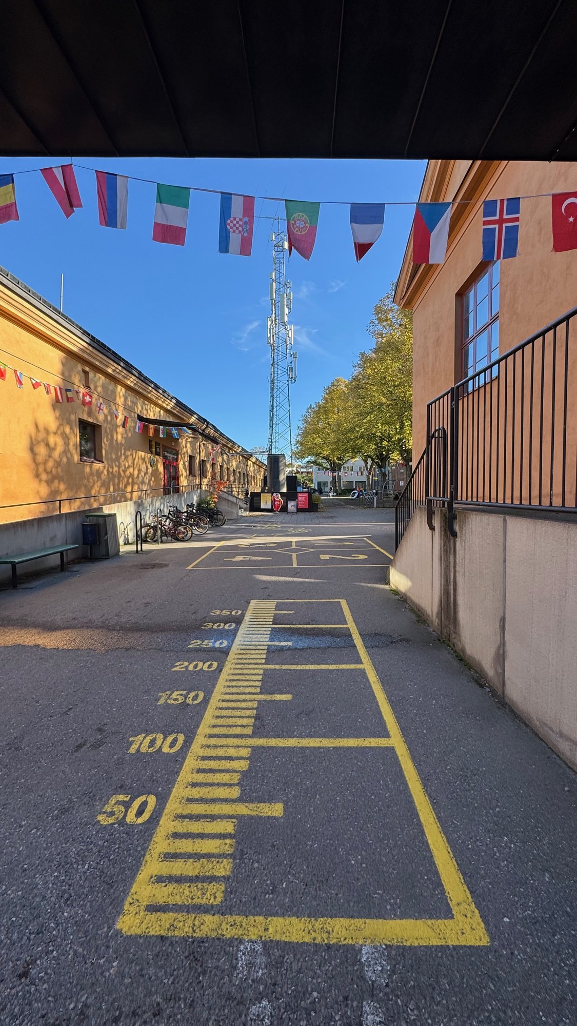 Yellow long jump marks painted on the street under flags outside Riksidrottsmuseet.