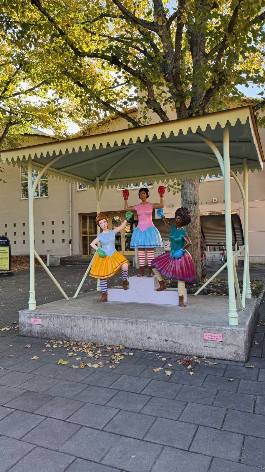 A colorful sculpture of three girls in a small pavilion outside Riksidrottsmuseet.
