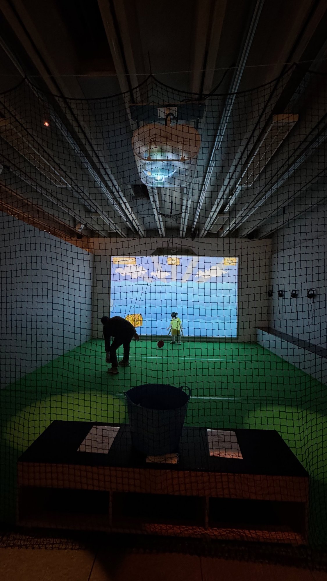 A room with a big screen and a green floor where visitors try a sport at Riksidrottsmuseet.