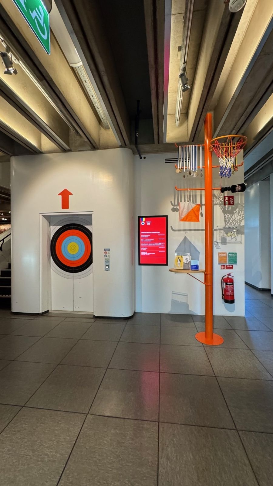 A lift door with an arrow sign and a target on the wall at Riksidrottsmuseet.