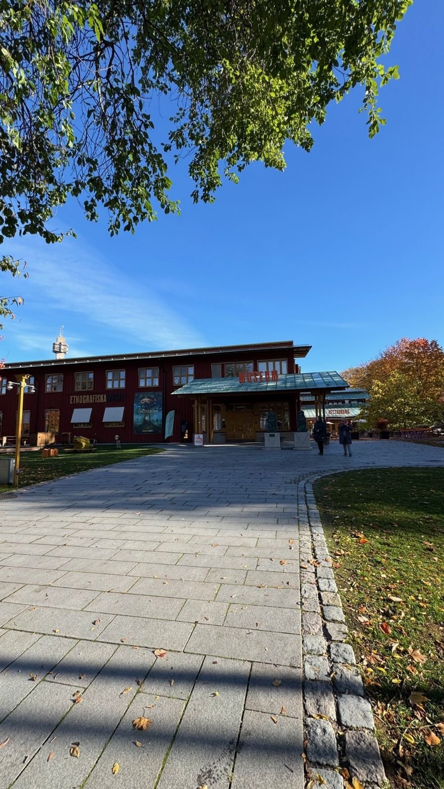 The red wooden building of Etnografiska museet with a stone path and autumn trees.