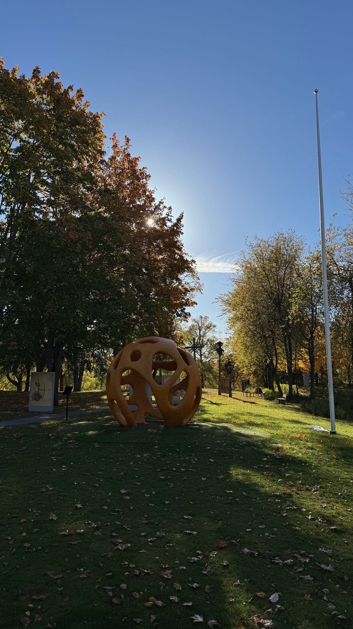 A large rusty metal sphere sculpture on the lawn at Etnografiska museet.