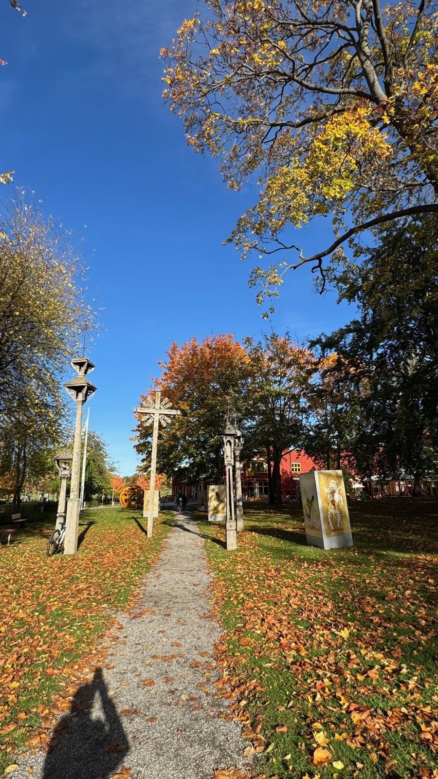 A gravel path with tall carved wooden poles and autumn leaves at Etnografiska museet.