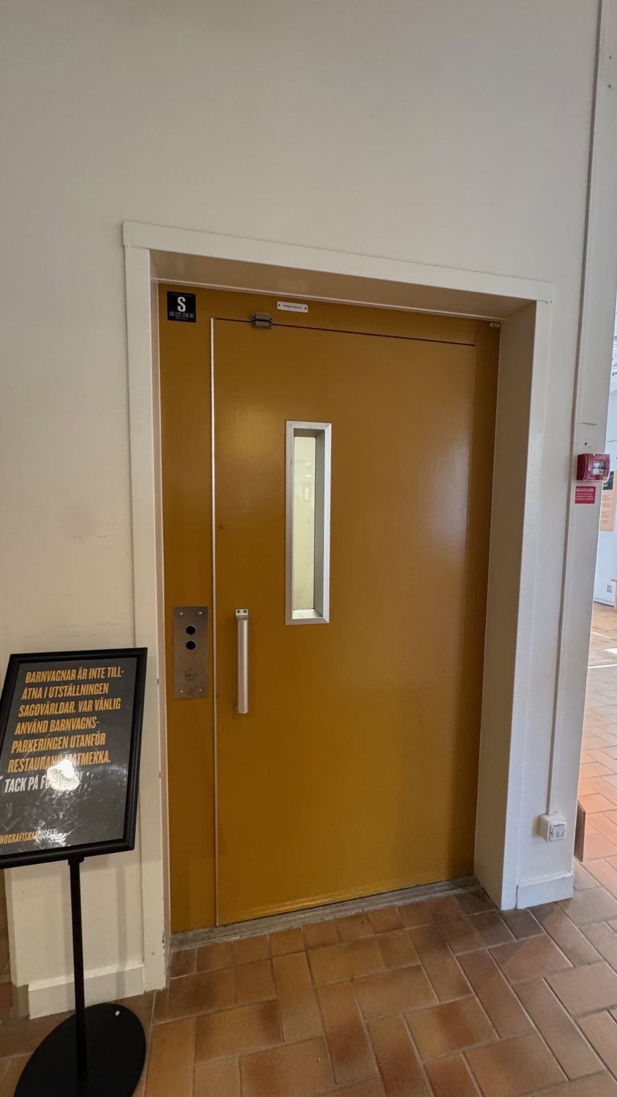A yellow lift door with a sign next to it at Etnografiska museet.