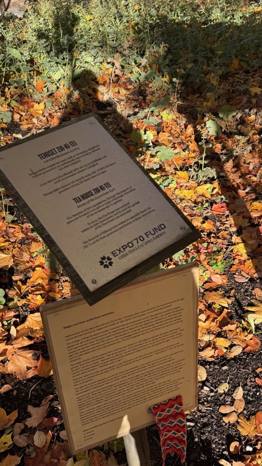 A metal plaque about the tea house Zui-Ki-Tei and a sign with a tea tale in the autumn leaves at Etnografiska museet.