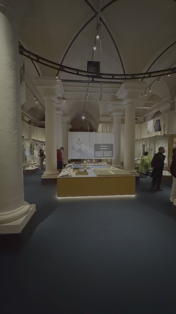 Vaulted exhibition hall at the Nobel Prize Museum, with white stone columns and glass display cases.