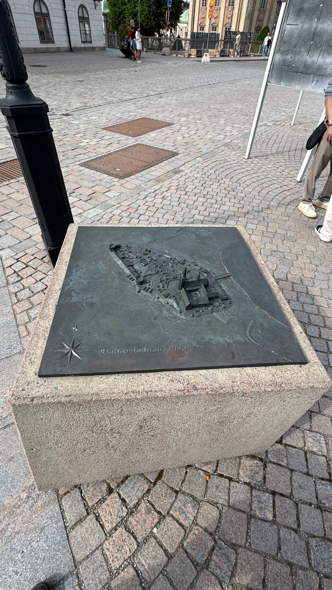 A bronze relief model of Riddarholmen in 1620, with the church and houses in miniature, on a stone block on a cobbled square.
