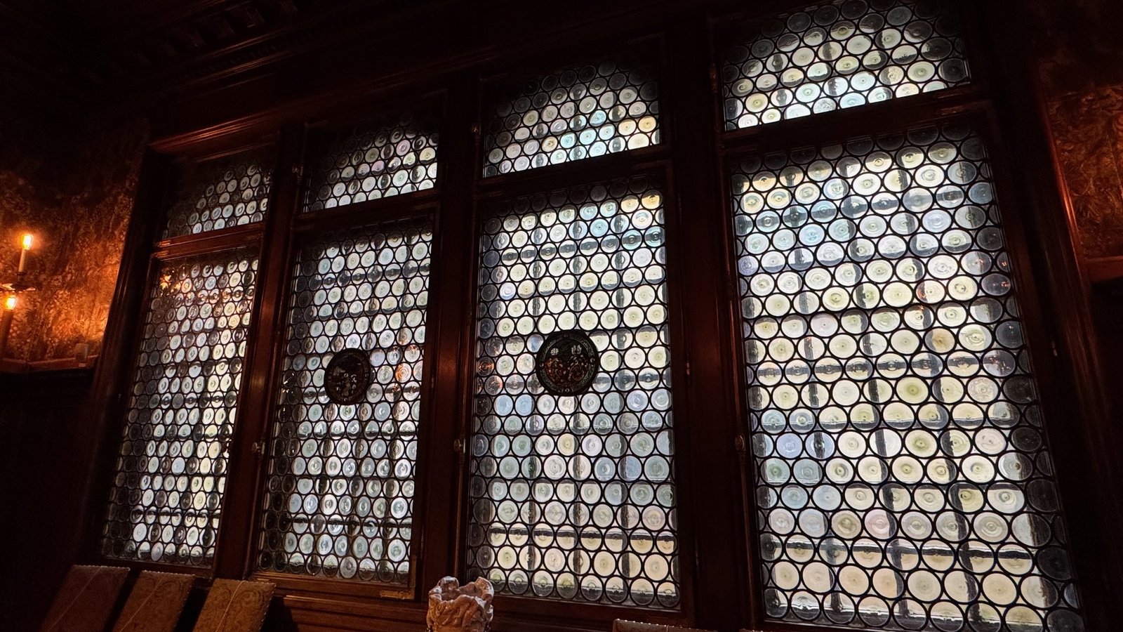 Tall leaded glass windows with round panes in a dark wooden room at the Hallwyl Museum.