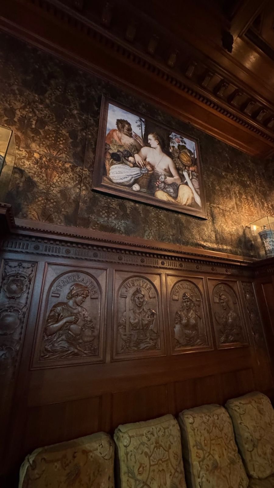 Carved wooden wall panels with figures of women, dark patterned walls and a painting above them at the Hallwyl Museum.