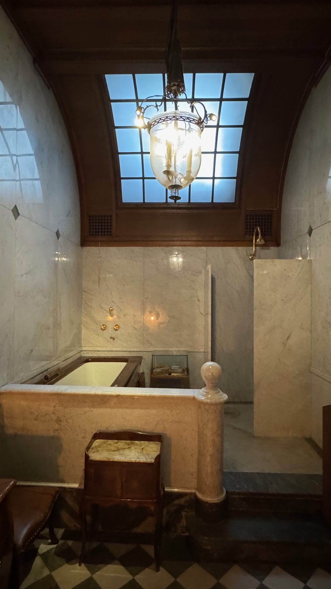 A marble bathroom with a bathtub, a shower and a skylight with a hanging lantern at the Hallwyl Museum.
