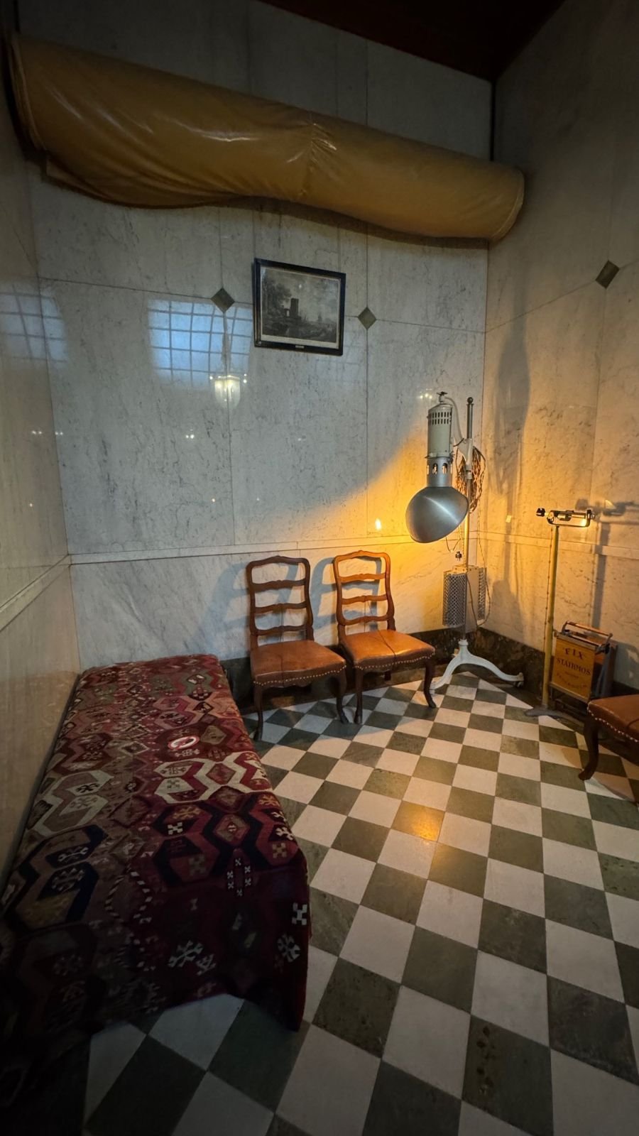 A room with a checkered stone floor, a daybed under a patterned rug, two chairs and an old lamp at the Hallwyl Museum.