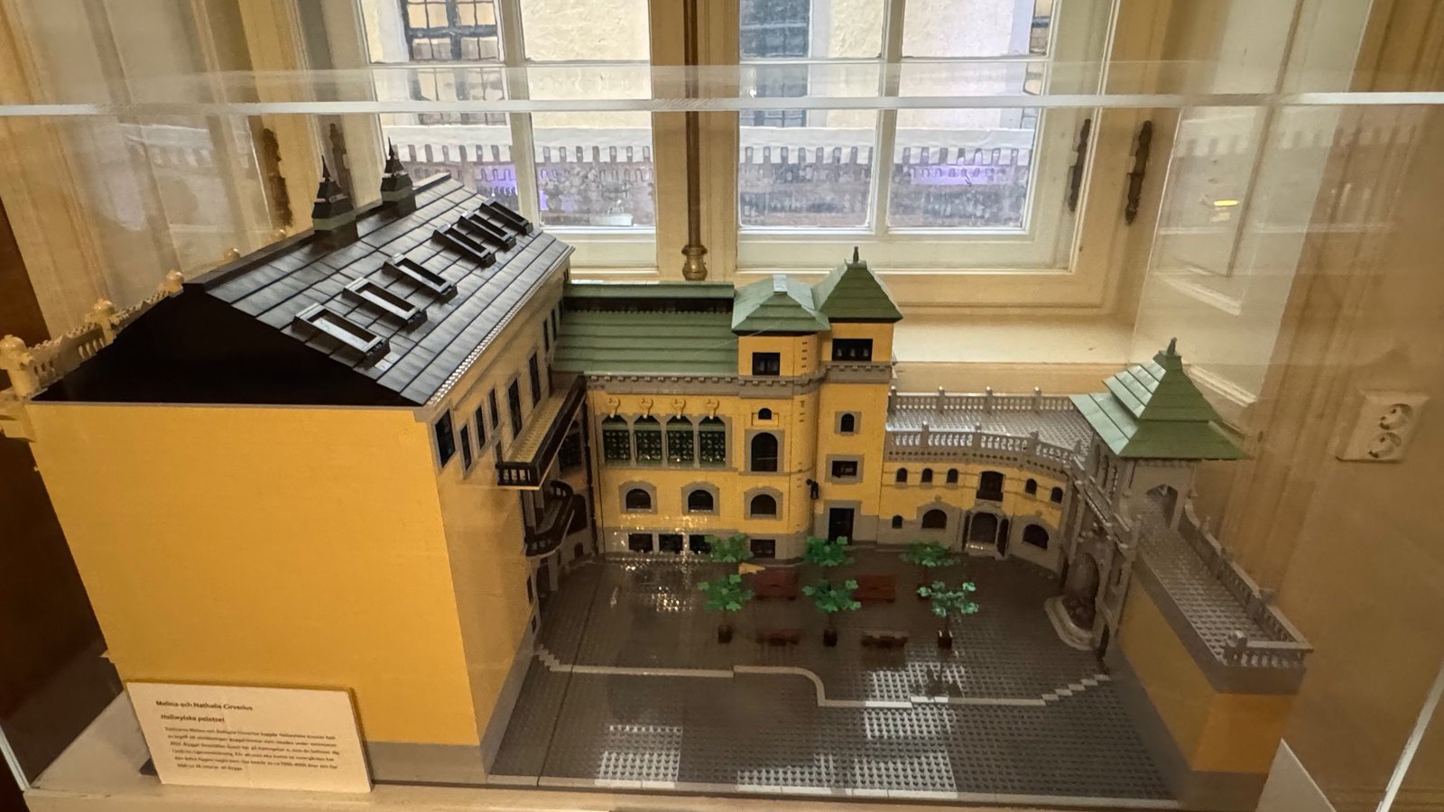 A model of the Hallwyl house built from toy bricks, with yellow walls, green roofs and the inner courtyard, in a glass case.