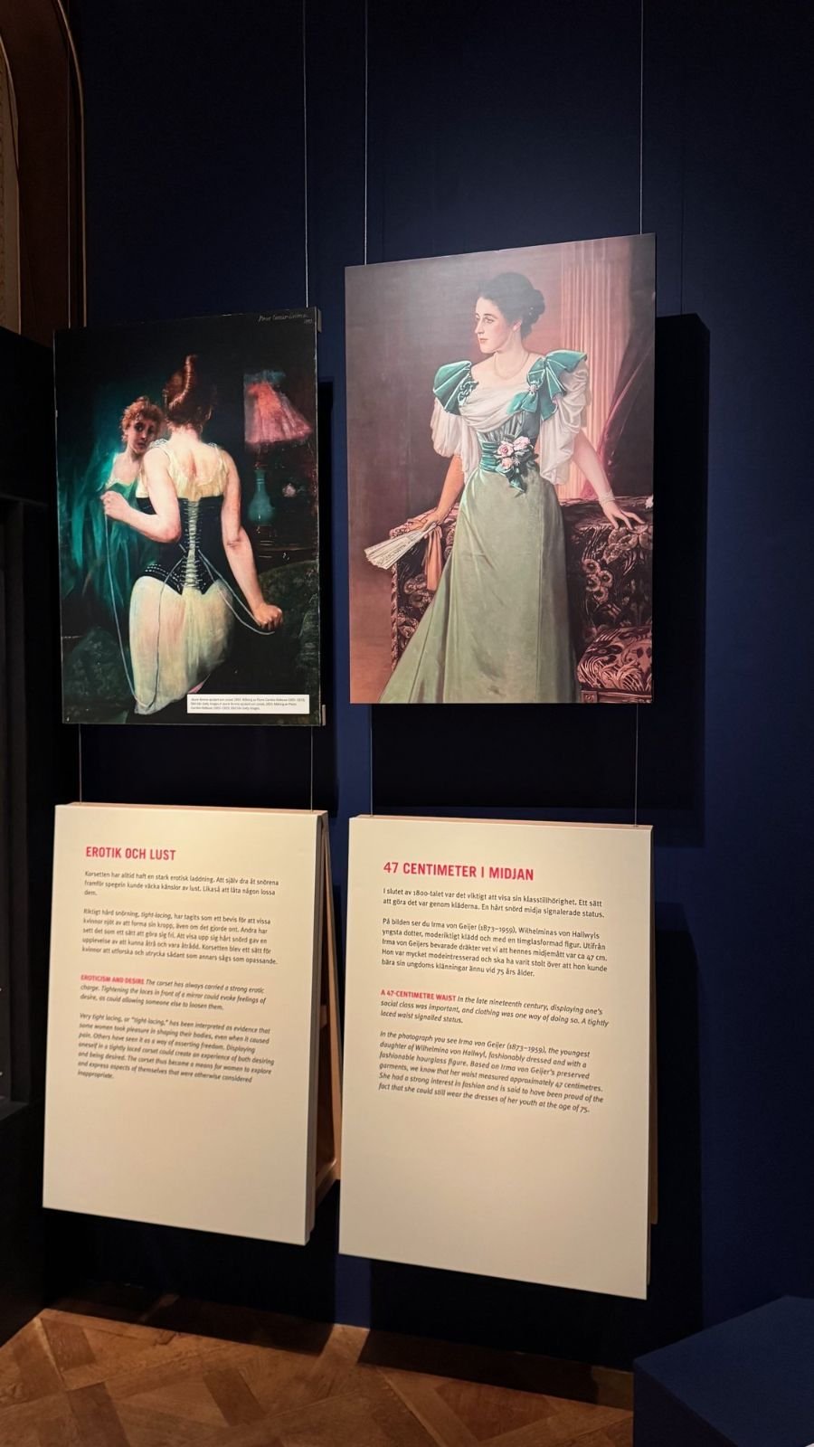 Pictures of women in corsets above text panels in Swedish and English on a dark blue wall at the Hallwyl Museum.
