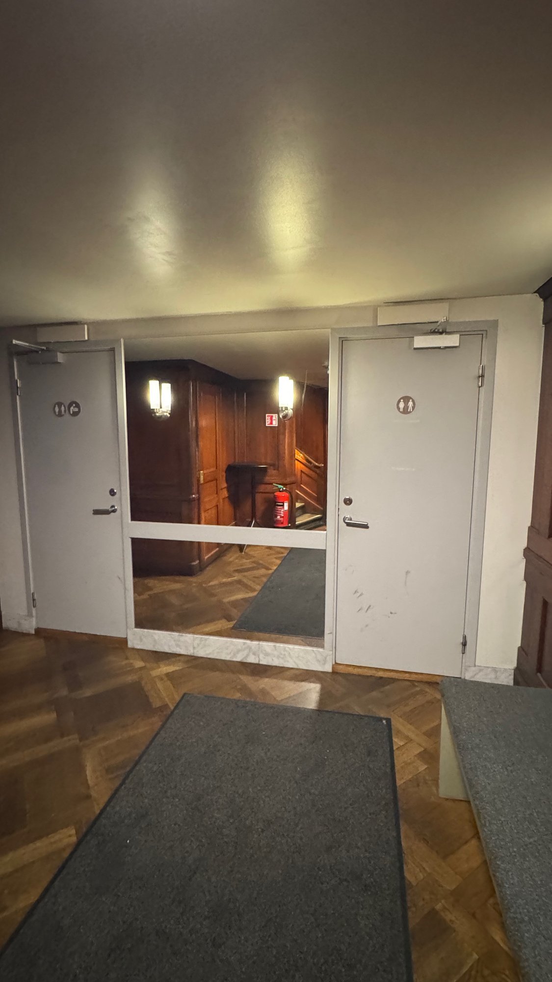 Two white toilet doors with signs, one with a baby changing sign, in a hall with a wooden floor at the Hallwyl Museum.
