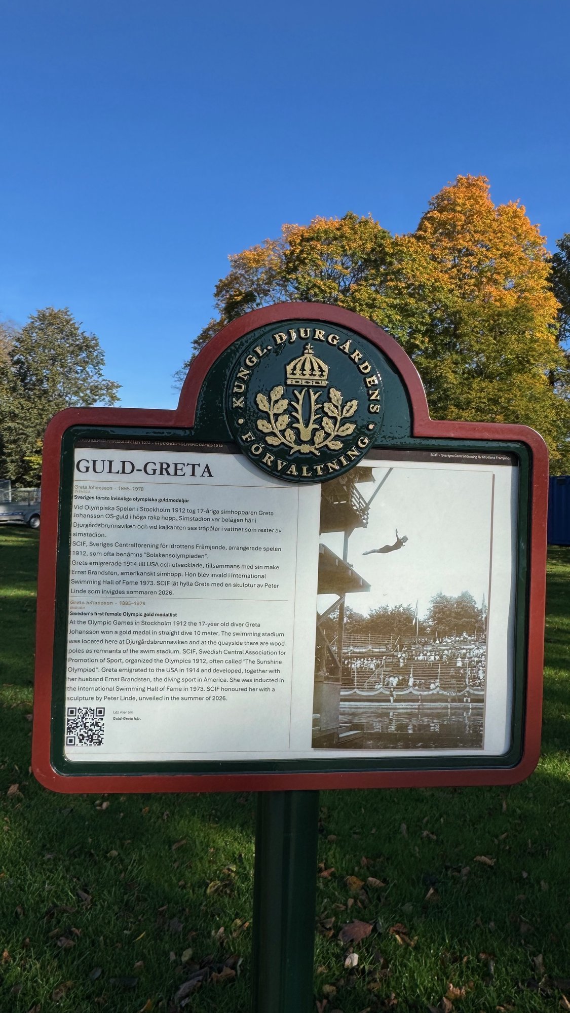 Information sign titled Guld-Greta, with text in Swedish and English and an old photo of a woman diving from a high tower.