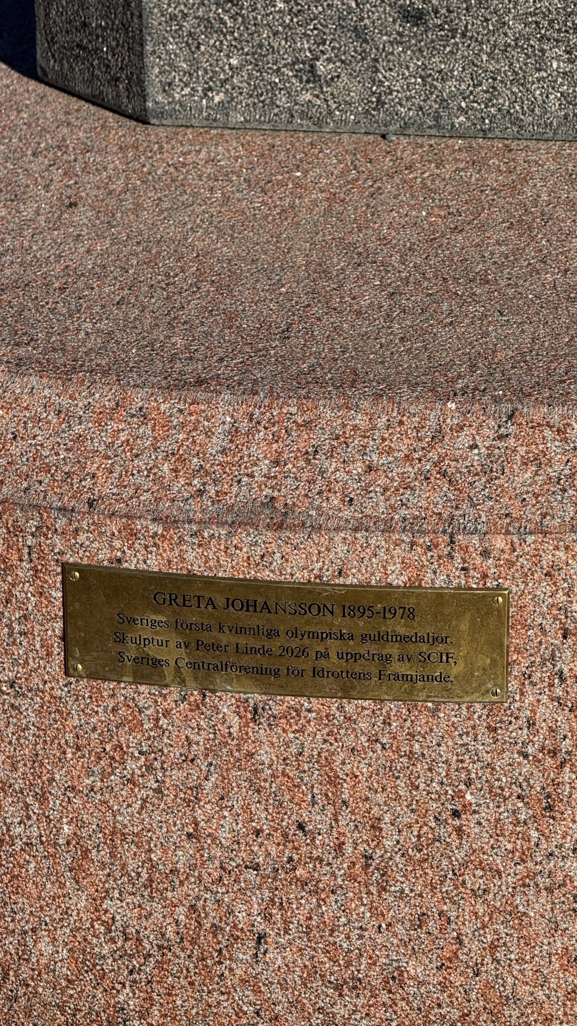 Brass plaque on a red granite base: Greta Johansson 1895-1978, Sweden's first female Olympic gold medalist, sculpture by Peter Linde 2026.