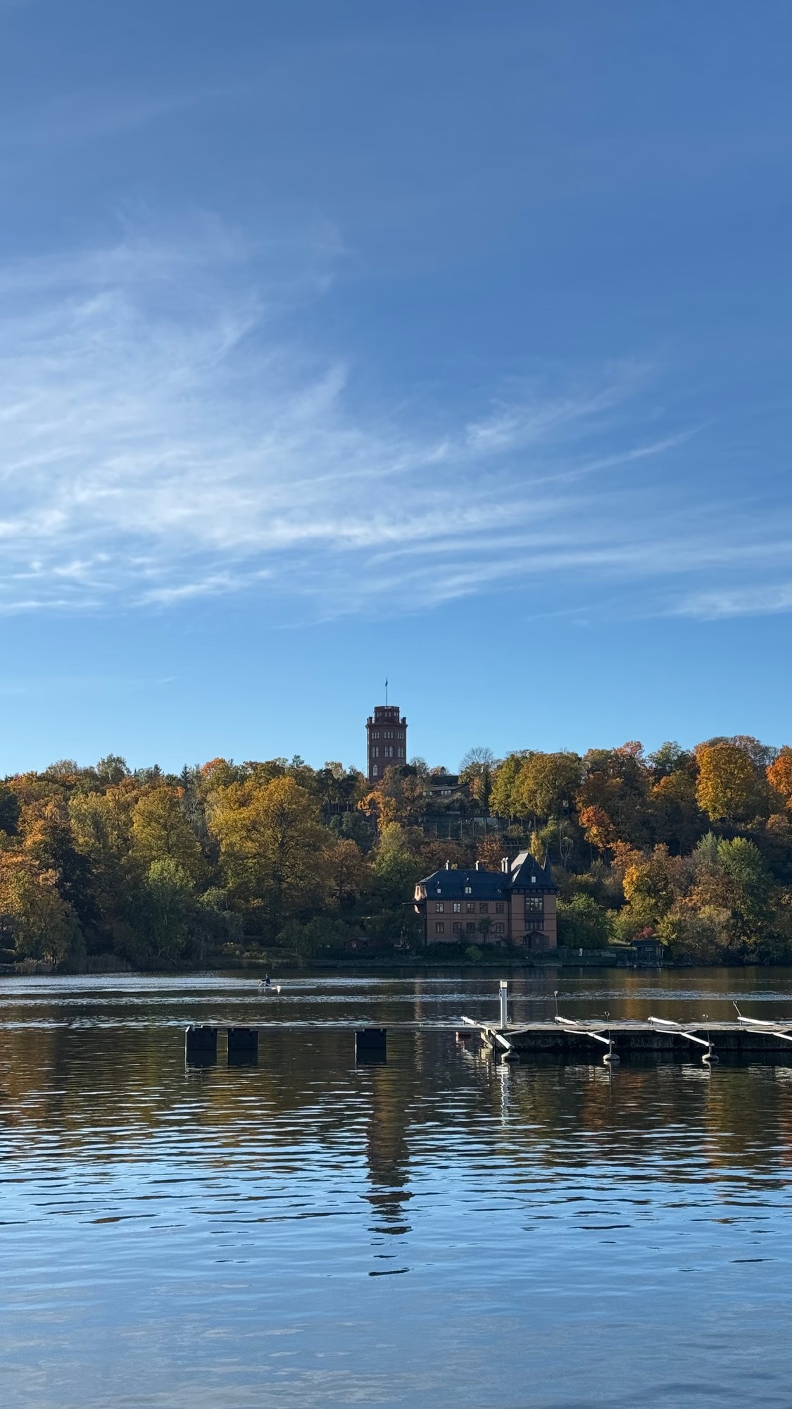 Djurgårdsbrunnsviken with a jetty in the water and autumn trees on the far shore.