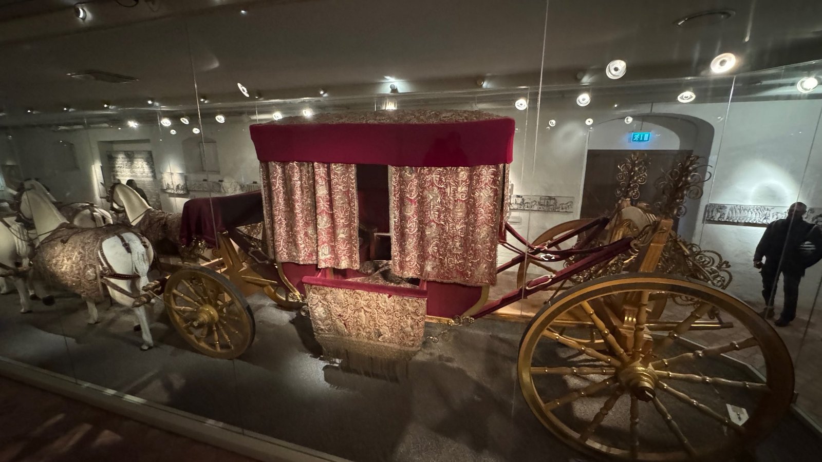 Queen Kristina's coronation coach from 1650 behind glass, with gilded wheels, red and gold embroidered curtains and white model horses in red and gold trappings.