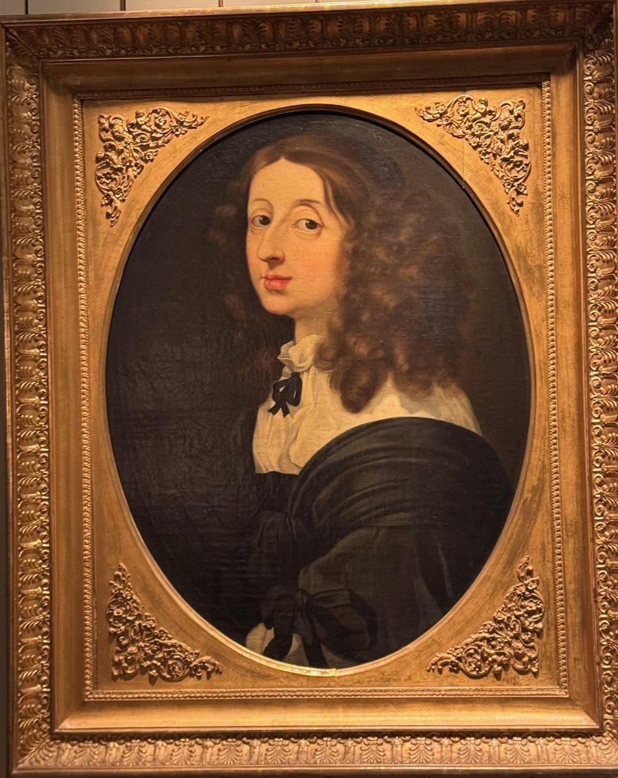Oval portrait of Queen Kristina with long brown curls and a black dress in a carved gilt frame, a copy after Sébastien Bourdon.