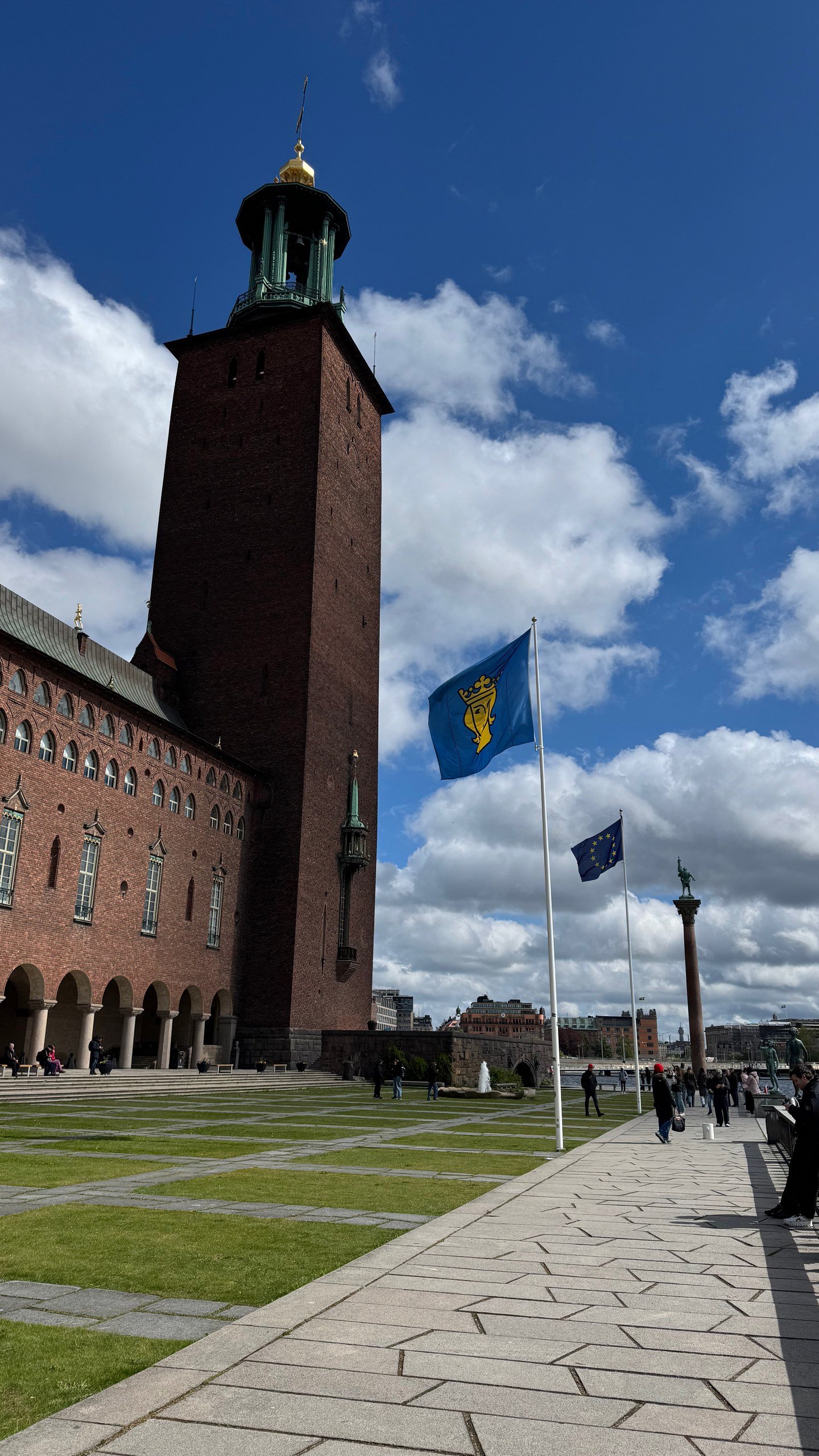 The tower of Stockholm City Hall against a blue sky, with the Swedish flag flying, photographed by Zayera Khan