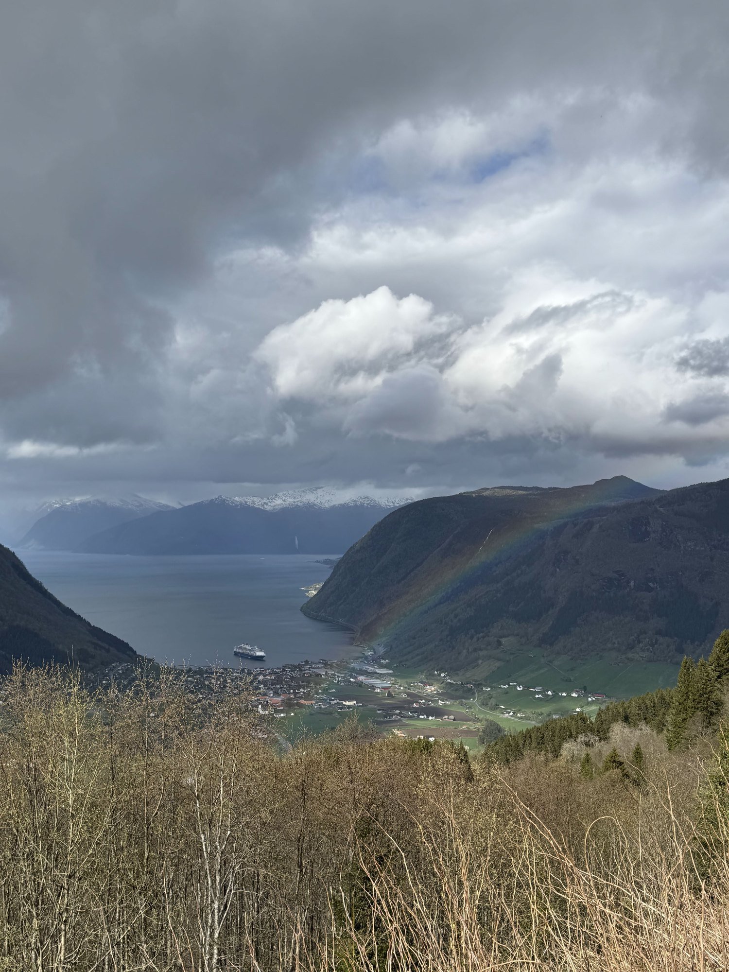 A rainbow over the Sognefjord, with dark clouds and a small town on the shore below.