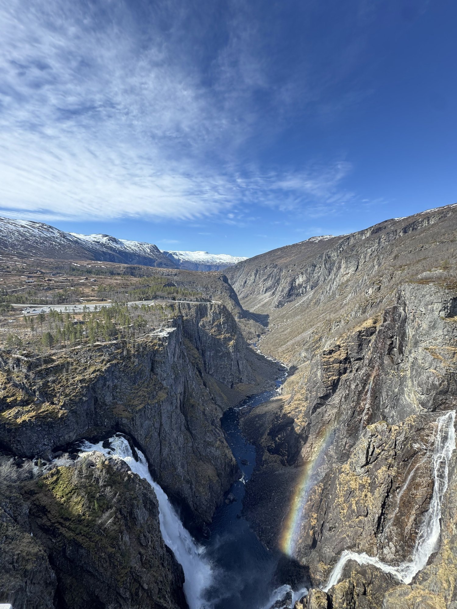 A deep gorge with a waterfall and a rainbow, seen from high above.