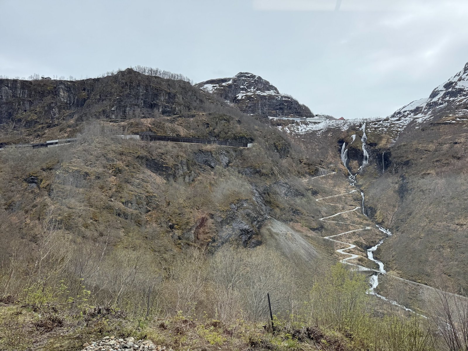 A road with many hairpin bends climbs a steep hillside between waterfalls.