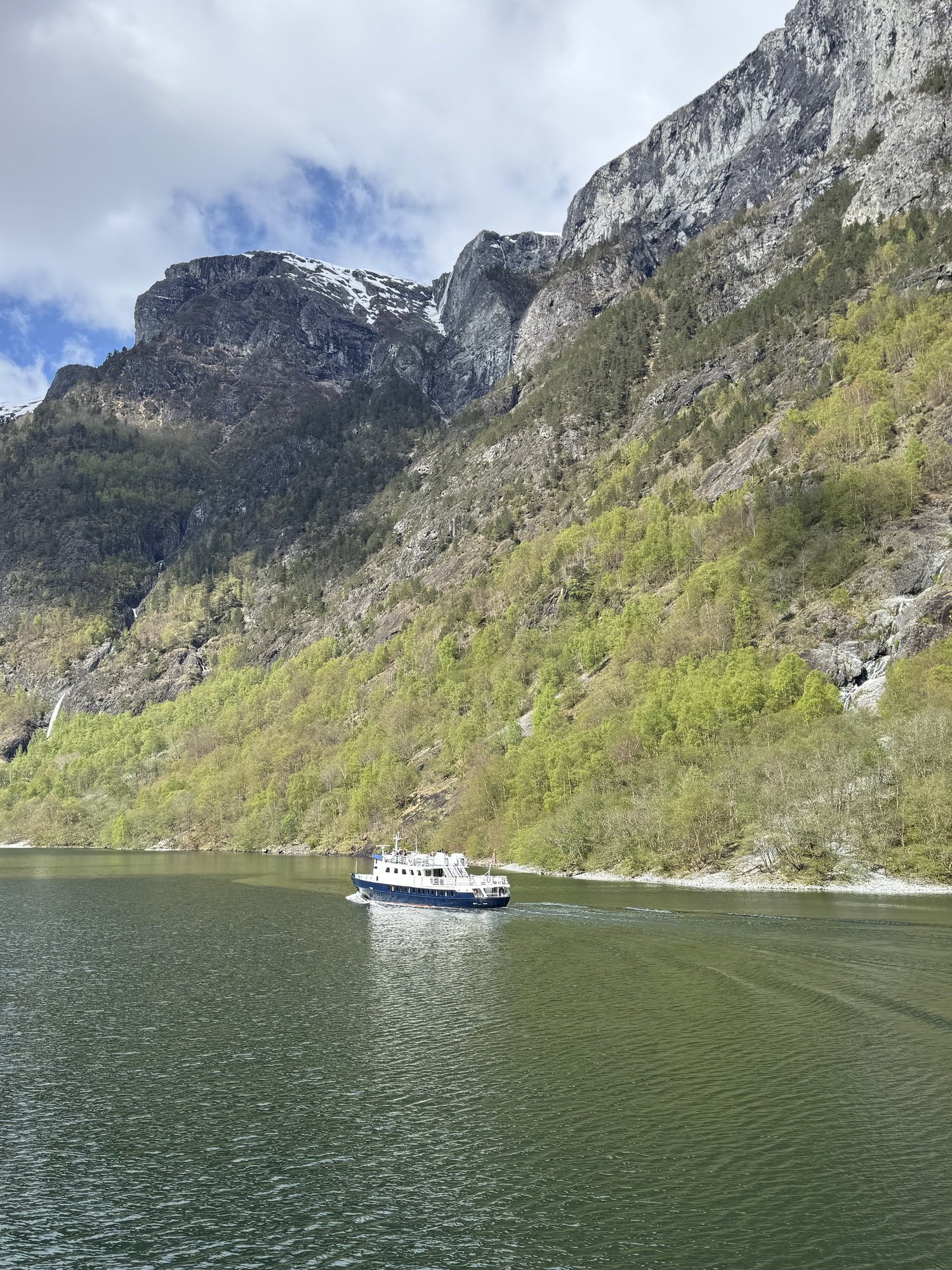 A small ferry on the green water of the Nærøyfjord, below steep cliffs.