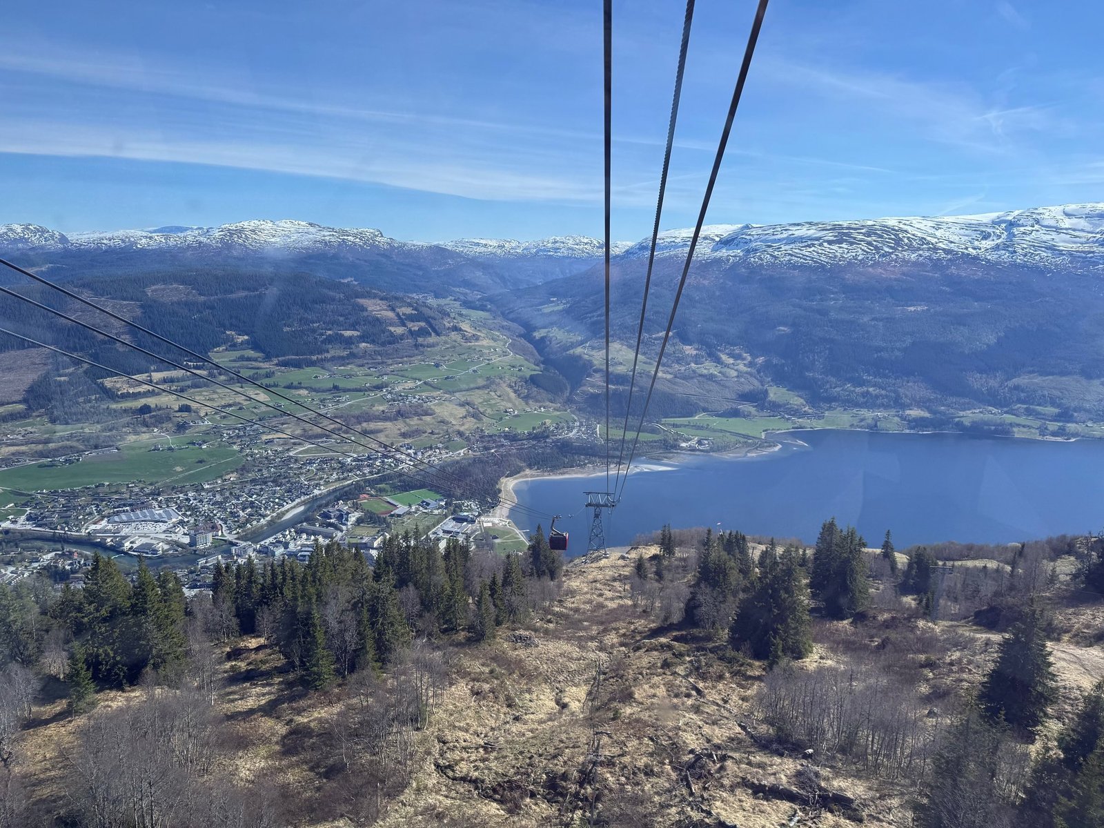Voss, its lake and the valley seen from high above, with gondola cables in front.