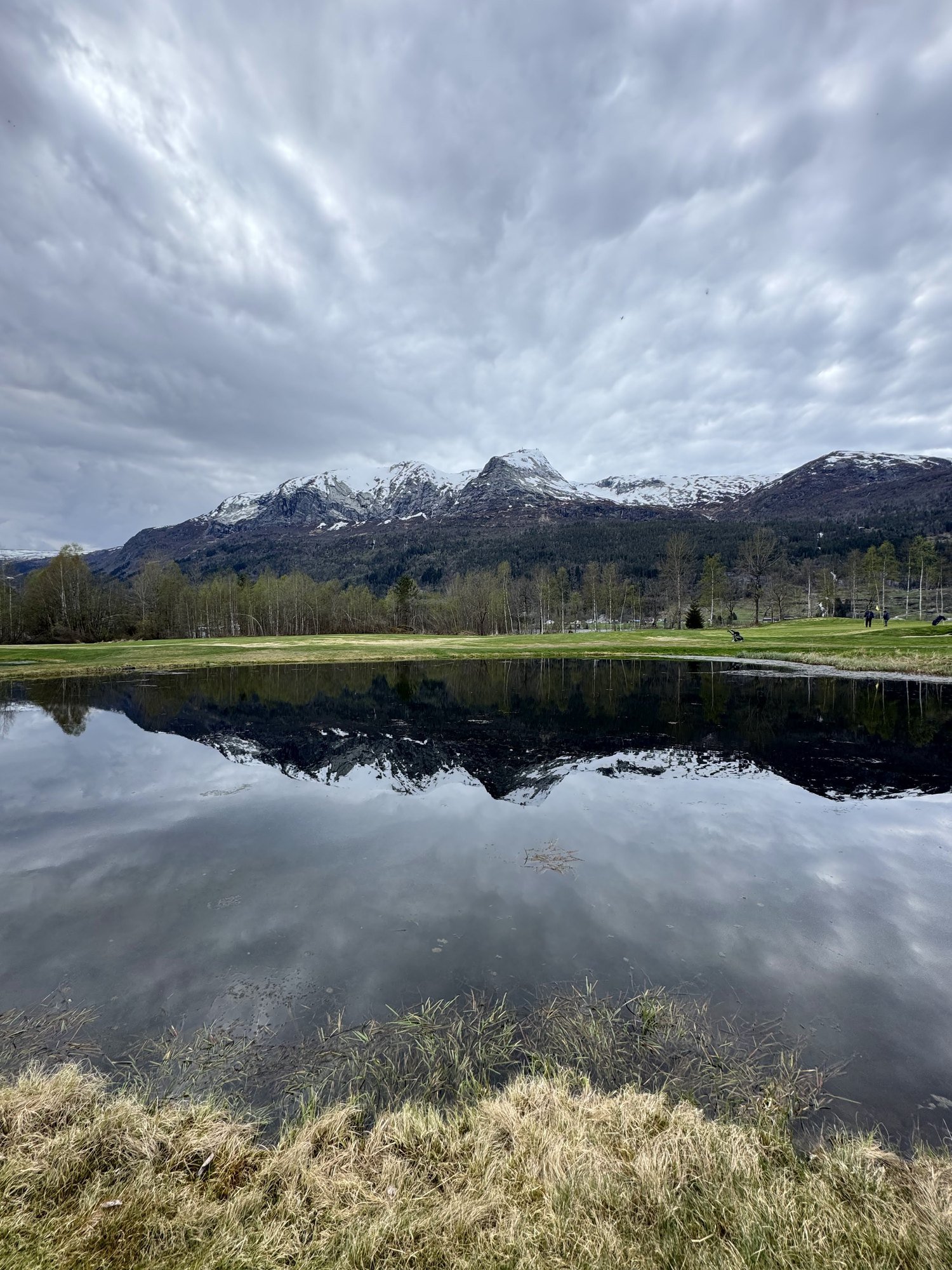 Snow-topped mountains reflected in a still lake under a cloudy sky.