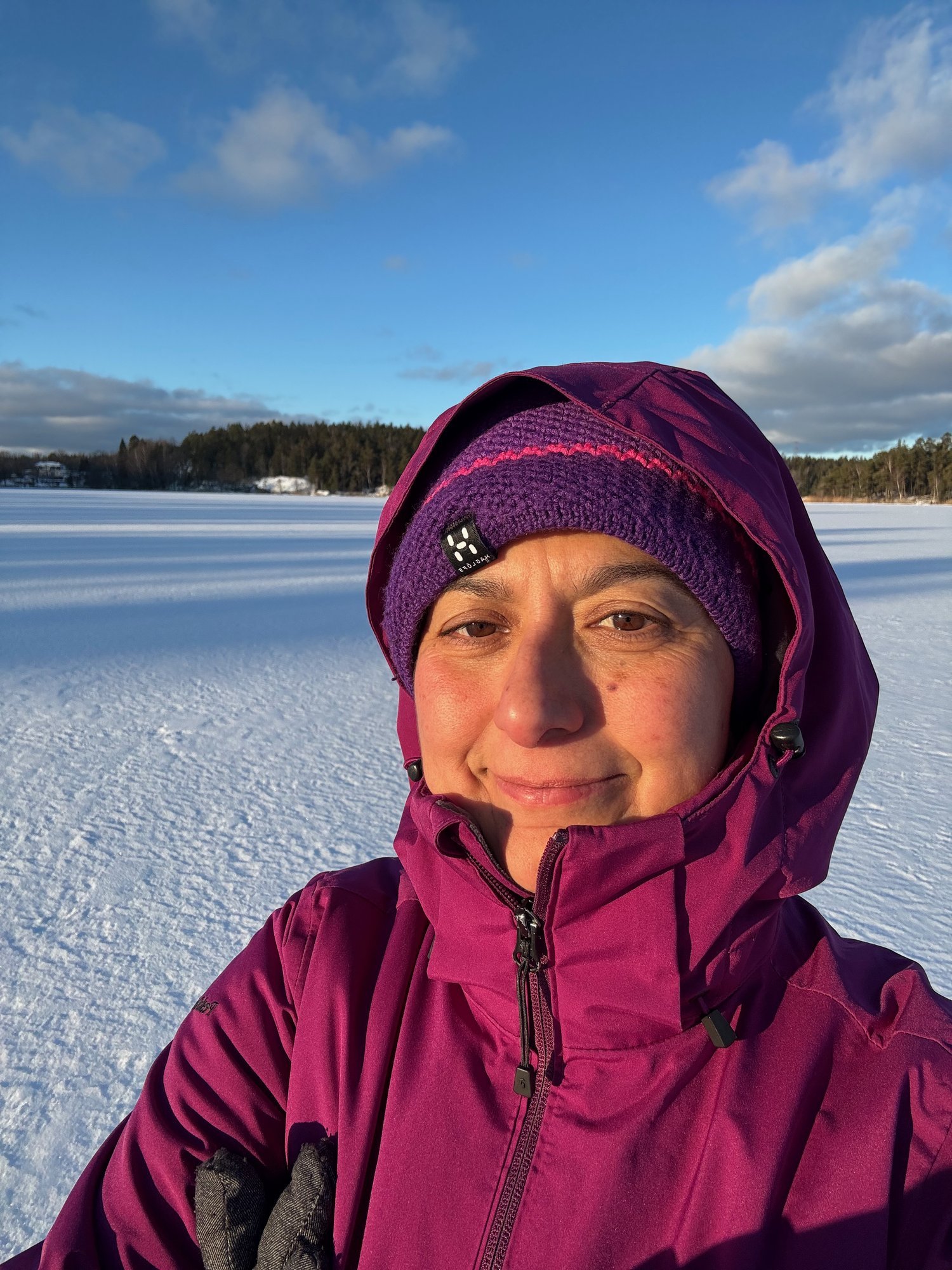Zayera Khan in a purple jacket and hat smiles on a snowy frozen lake under a blue sky.